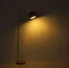 A floor lamp is shown in a dimly lit room, casting a warm glow on the wall. Produktbild-Vorschau