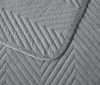 A close-up view of a gray quilted blanket with a chevron pattern. Podgląd zdjęcia produktu