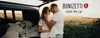 A couple embracing in front of an open car trunk, with a field in the background. Produktbild-Vorschau
