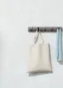 A beige tote bag and a blue towel hang from a gray hook rack mounted on a textured light gray wall. Náhľad obrázku produktu