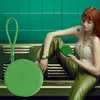 A young woman with red hair is sitting and holding a green smartwatch and a matching green round case. Produktbild-Vorschau