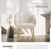 A cream-colored armchair with gold legs is displayed in a well-lit room with soft shadows. A vase with branches is placed to the left of the chair. Produktbild-Vorschau