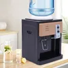 A desktop water dispenser with a water bottle on top, placed on a wooden countertop next to a pitcher of water, a glass, and a lemon. Náhled obrázku produktu