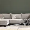A cordless vacuum cleaner is placed on a rug in front of a sofa in a living room. Produktbild-Vorschau