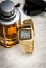 A gold Casio watch is placed next to a bottle of cologne on a white fluffy surface. Produktbild-Vorschau