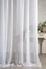 A white voile curtain hangs in front of a brick wall and a piece of furniture. Produktbild-Vorschau