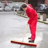 A man in a red jumpsuit is sweeping a wet asphalt surface with a large broom. Produktbild-Vorschau