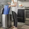 A woman is placing a blue bin into a stainless steel trash can in a kitchen. Podgląd zdjęcia produktu