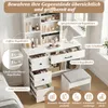 A white vanity table with drawers and shelves, filled with cosmetics and accessories, placed near a window. A stool is in front of the table. Náhled obrázku produktu