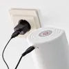A white automatic water dispenser is being charged via a USB cable connected to a black power adapter plugged into a white wall socket. Náhľad obrázku produktu