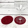 Two red felt coasters with angel and star cutouts are shown on a white wooden surface. A wine glass is placed on one of the coasters. Produktbild-Vorschau