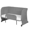 A gray baby crib/bed with a mattress, shown from a front-side angle on a white background. Anteprima dell’immagine prodotto