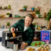 Jamie Oliver in a kitchen setting with his air fryer and cookbook. Produktbild-Vorschau