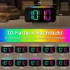 A digital alarm clock with multiple color options for its night light feature, displayed on a table with books in the background. Produktbild-Vorschau