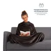 A woman is sitting on a couch, wrapped in a blanket with sleeves, and reading a book. Podgląd zdjęcia produktu