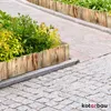 A wooden garden border is used to edge a planter with green and yellow foliage, set against a cobblestone pathway. Náhled obrázku produktu