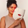 A woman is holding a white LED face mask in front of her face, with the red light from the mask illuminating her skin. Anteprima dell’immagine prodotto