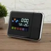 A digital alarm clock with weather projection features is displayed on a wooden surface. Náhled obrázku produktu