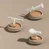 Three parts of a balance bike (handlebars, frame, and seat) are displayed on separate beige circular bases against a plain beige background. Náhled obrázku produktu
