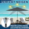 A dark gray patio umbrella is set up on a sandy beach with lounge chairs and the ocean in the background. The image highlights the umbrella's adjustable tilt feature and its ability to provide shade from the sun. Voir les images du produit