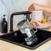 A person is filling a water filter pitcher under a black faucet in a kitchen sink. Podgląd zdjęcia produktu