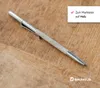 A metal marking tool with a knurled grip and a pointed tip rests on a wooden surface. A white overlay in the top right corner contains text and a checkmark, and a brand logo is visible in the bottom right corner. Produktbild-Vorschau