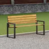A wooden bench with black metal legs is shown outdoors on a gravel path, with a grassy area and a stone and wood fence in the background. Náhled obrázku produktu