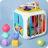 A colorful activity cube toy with various shapes and gears on top, placed on a light blue background. Produktbild-Vorschau