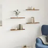 Four wooden shelves mounted on a white wall, decorated with books and a plant. A blue armchair is visible on the right. Produktbild-Vorschau