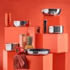 A collection of Tefal cookware and kitchen accessories arranged on orange blocks against an orange background. Produktbild-Vorschau