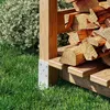 A close-up view of a wooden log holder with stacked firewood, set against a backdrop of green grass and foliage. Náhled obrázku produktu