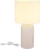 A white table lamp with a textured glass base and a white fabric shade, shown on a white background with its power cord and plug visible. Anteprima dell’immagine prodotto