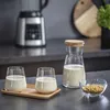 A kitchen counter with a blender in the background and a carafe of milk, two glasses of milk, and a bowl of seeds in the foreground. Voir les images du produit