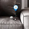 A white keychain accessory is placed on a textured gray couch, with a blue location pin overlay pointing to it. Produktbild-Vorschau