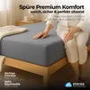A person sitting on a bed with a grey fitted sheet. Náhľad obrázku produktu
