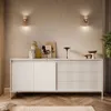 A modern living room setting with a white sideboard, decorative items, and wall sconces. Produktbild-Vorschau