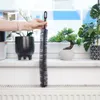 A hand holding a long brush over a radiator, with plants on a windowsill in the background. Podgląd zdjęcia produktu