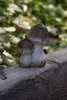 A ceramic mushroom decoration sits on a stone ledge with greenery in the background. Produktbild-Vorschau