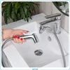 A hand with red nail polish is holding a bidet shower head over a white sink, with a faucet in the background. Náhľad obrázku produktu