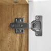 A close-up view of a cabinet hinge attached to a wooden surface and a white surface. Voir les images du produit