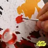 A close-up of a person's hand painting a "paint by numbers" canvas with acrylic paints. Produktbild-Vorschau