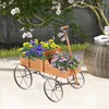 A wooden wagon filled with colorful flowers sits on a patio, with a tree and a woven table in the background. Voir les images du produit