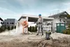 A construction worker is using a pressure washer to clean a cement mixer on a construction site. Náhled obrázku produktu