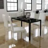 A dining set with a black table and white chairs in a bright, modern room with large windows. Náhled obrázku produktu