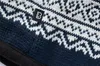 A close-up view of a knitted hat with a navy and white pattern and a brand logo. Náhled obrázku produktu