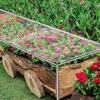 A close-up view of a garden planter box filled with colorful flowers, covered by a transparent protective tarp. Náhled obrázku produktu