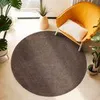 A round rug is placed on a light-colored floor next to a yellow armchair and potted plants. Produktbild-Vorschau
