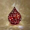 A red decorative lamp shaped like a teardrop with star cutouts, casting star-shaped light patterns on a textured background. Produktbild-Vorschau