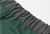 A close-up view of the elastic waistband of a pair of green shorts with a gray fabric overlay. Produktbild-Vorschau