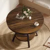 A round wooden table with a vase of flowers, a book, a candle, and a cup of coffee on it, placed on a woven rug. Produktbild-Vorschau
